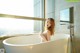 A woman sitting in a bathtub in front of a window.