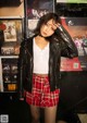 A woman in a leather jacket and plaid skirt posing for a picture.