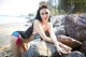 A woman in a bikini sitting on a rock on the beach.