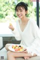 A woman sitting on a couch holding a plate of fruit.