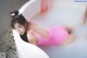 A woman in a pink bathing suit laying in a bathtub.