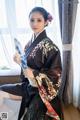 A woman in a black kimono sitting on a couch holding a fan.