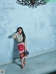 A woman standing in front of a blue wall holding a handbag.