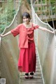 A woman in a red dress standing on a rope bridge.